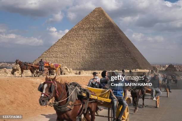 People ride on carriages past the pyramids of Khufu at the Giza pyramids necropolis on the southwestern outskirts of the Egyptian capital Cairo, on...