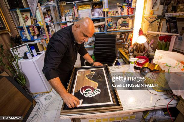 Iraqi calligrapher Wael al-Ramadan wipes the glass on one of his Arabic calligraphy framed art pieces at his workship in al-Ashar district of Iraq's...