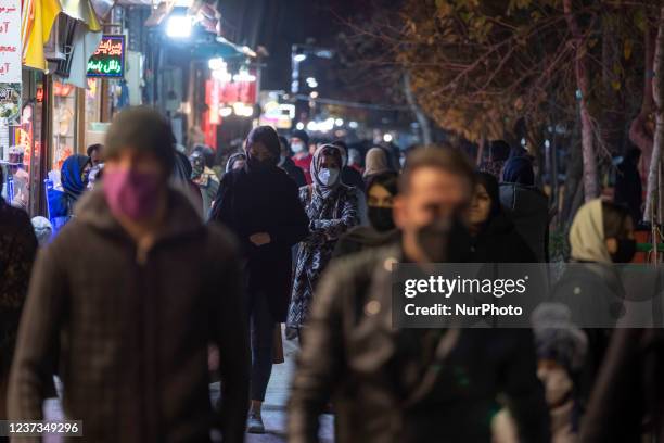 An Iranian woman wearing a protective face mask looks on while walking along a street-side in the city of Isfahan, 450 km south of Tehran, at night...