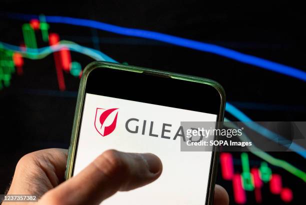 In this photo illustration the American biotechnology company Gilead Sciences logo seen displayed on a smartphone with an economic stock exchange...
