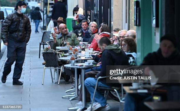 Pedestrian wearing a face covering to combat the spread of Covid-19, passes customers enjoying drinks outside a restaurant in the Soho district of...