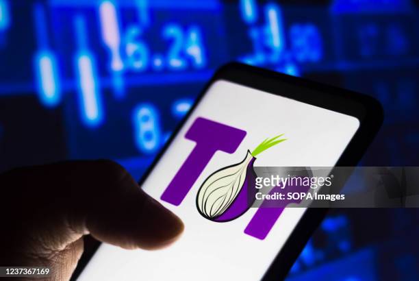 In this photo illustration, a hand is seen holding a smartphone that displays the Tor browser logo.