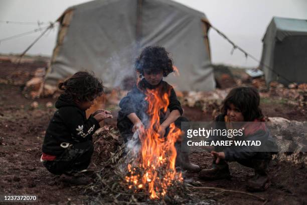 Children from the Syrian family of Abou Hussein, who fled the countryside of Hama province four years prior, warm up around a bonfire of burning...