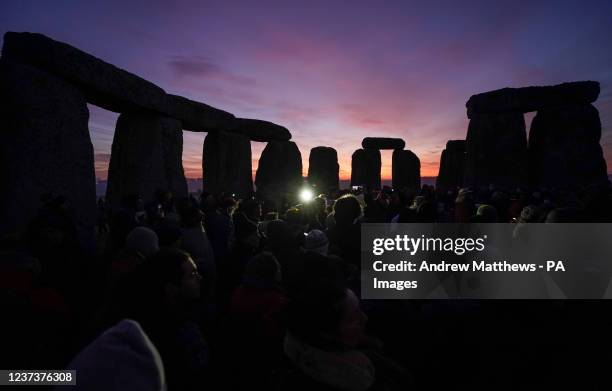 The sun begins to rise behind the stones as people gather to take part in the winter solstice celebrations during sunrise at the Stonehenge...
