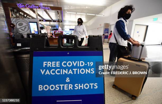 Travelers walk past a sign offering free Covid-19 vaccinations and booster shots at a pop-up clinic in the international arrivals area of Los Angeles...