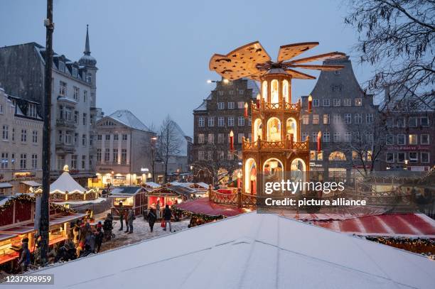 December 2021, Schleswig-Holstein, Flensburg: In the afternoon, when snow falls, people visit the Christmas market with the large Christmas pyramid....