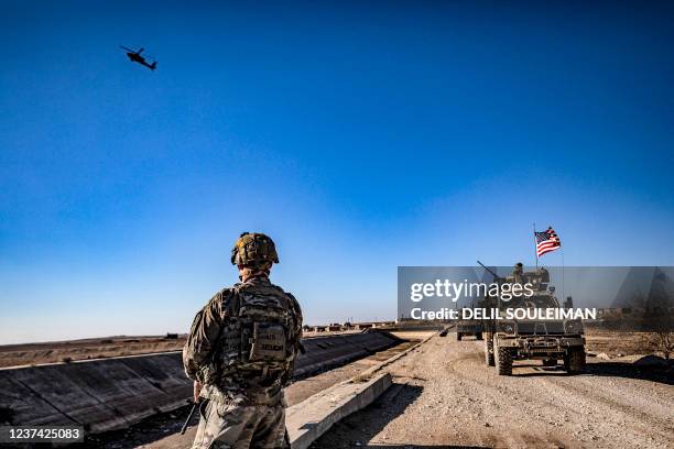 Apache attack helicopter flies above US soldiers patrolling along the frontlines between areas held by the Syrian Democratic Forces and...