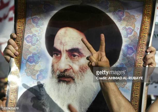 Sign for victory is flashed in front of a portrait of religious leader of Iraq's Shiite majority Grand Ayatollah Ali al-Sistani during a march...