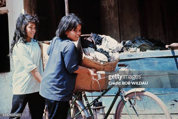 Two young Vietnamese girls carry a cardboard box on their bikes in the streets of Kuong Tung during the Vietnam War in 1967.