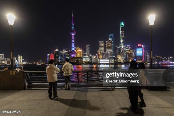 Pedestrians walk along the Bund past illuminated buildings in the Lujiazui Financial District across the Huangpu River at night in Shanghai, China,...