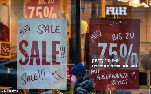 Woman wearing a face mask walks past a clothing retail shop offering sales in Berlin on December 29, 2021. Germain retailers owning "brick and...