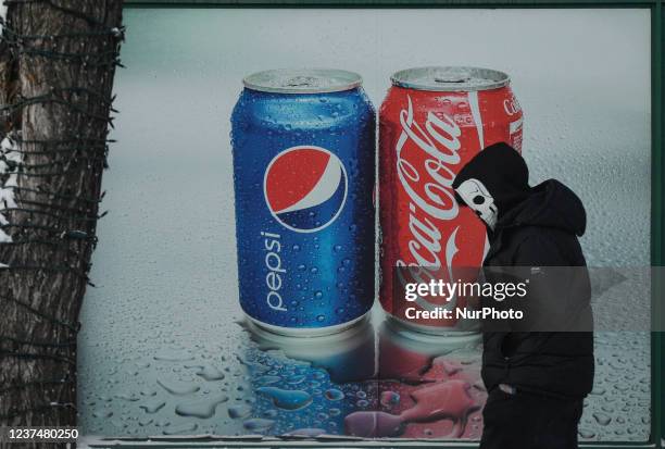 Man wearing a skull face mask walks past a Pepsi and Coca-Cola ad in the center of Edmonton. On Thursday, December 30 in Edmonton, Alberta, Canada.