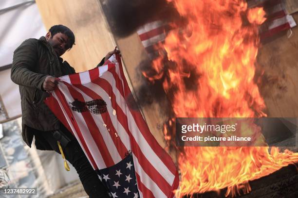 December 2021, Iraq, Baghdad: A man burns the US flag during a rally staged by supporters of Asa'ib Ahl al-Haq Shia group and the Iran-backed...