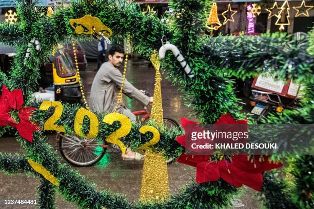 Man rides a scooter past Christmas decorations reading "2022" on display at a shop exhibiting Christmas accessories outside along a main street in...