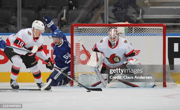 Tim Stutzle of the Ottawa Senators clears a puck for teammate Matt Murray against Michael Bunting of the Toronto Maple Leafs during an NHL game at...