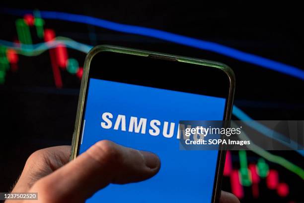In this photo illustration the South Korean multinational electronics conglomerate Samsung logo seen displayed on a smartphone with an economic stock...