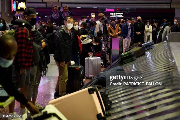 Airline passengers wearing face masks wait to collect bags from a baggage carousel at the Harry Reid International Airport on January 2, 2022 in Las...