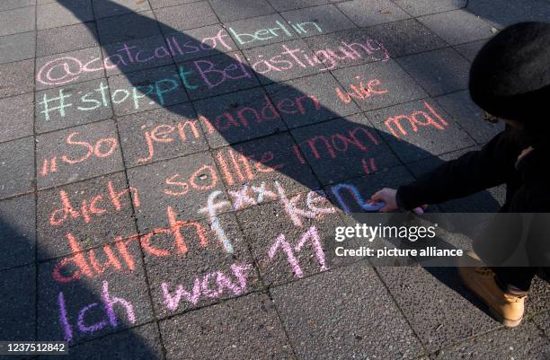 December 2021, Berlin: Student Lucie writes with chalk "@catcallsofberlin - #stopptästigung - "Jemanden wie dich sollte man mal ordentlich...