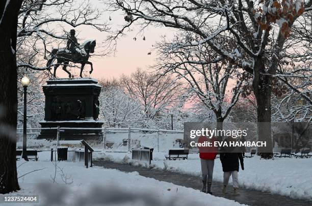 People walk through snow-covered Logan Circle in Washington, DC on January 3, 2022. - A winter storm hammered the capital and other parts of the...