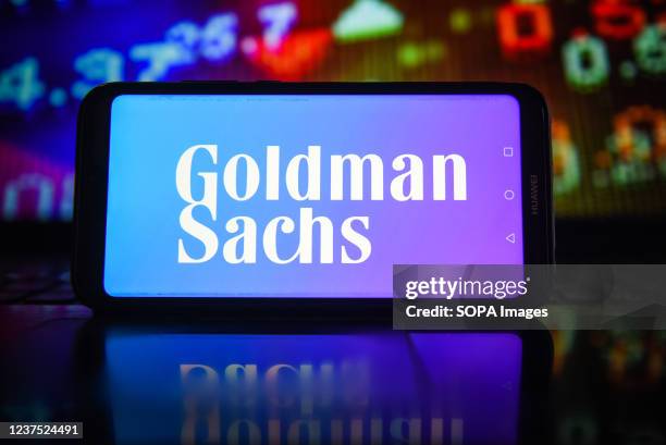 In this photo illustration a Goldman Sachs logo seen displayed on a smartphone with stock market percentages in the background.