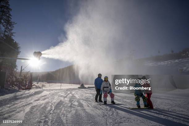 Snowboarders ride past a snow cannon at Wanlong Ski Resort in the Chongli district of Zhangjiakou, Hebei Province, China, on Monday, Jan. 3, 2022....