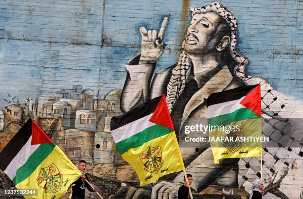 Masked members of the Fatah movement walk with flags of Palestine and Fatah past a mural depicting late Palestinian leader Yasser Arafat during a...