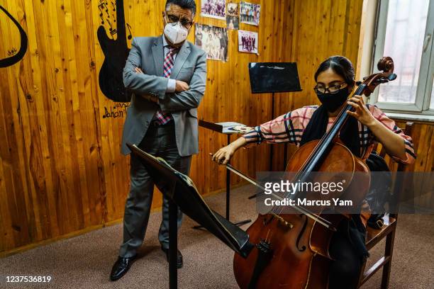 Dr. Ahmed Sarmast watches Meena practice the Cello at Afghanistan National Institute of Music in Kabul, Afghanistan, Sunday, May 2, 2021.