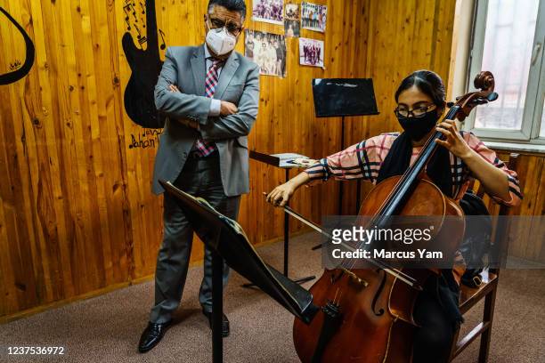 Dr. Ahmed Sarmast watches Meena practice the Cello at Afghanistan National Institute of Music in Kabul, Afghanistan, Sunday, May 2, 2021.
