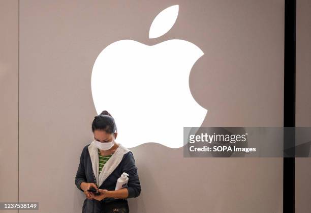 Woman wearing a face mask is seen using a smartphone as she stands in front of the American multinational technology company Apple logo and store in...