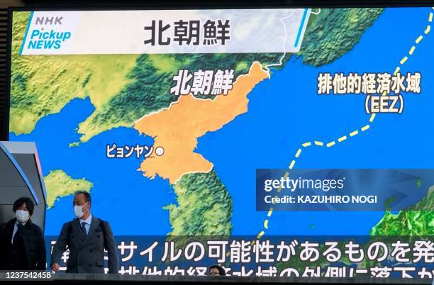 Pedestrians walk past a screen displaying a map after North Korea fired what appeared to be a ballistic missile into the sea off its east coast...