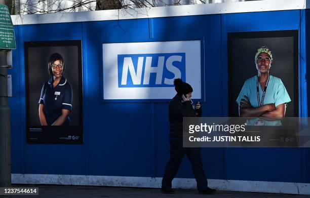 Pedestrians walk past images of workers of Britain's National Health Service fixed to hoardings outside a temporary field hospital, set up in the...