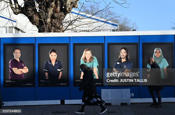 Pedestrians walk past images of workers of Britain's National Health Service fixed to hoardings outside a temporary field hospital, set up in the...