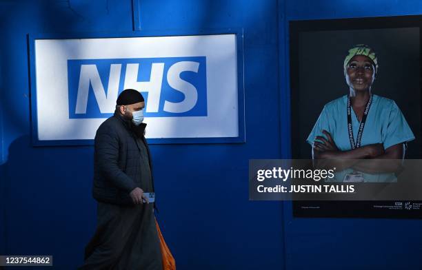 Pedestrians walk past images of workers of Britain's National Health Service fixed to hoardings outside a temporary field hospital, set up in the...