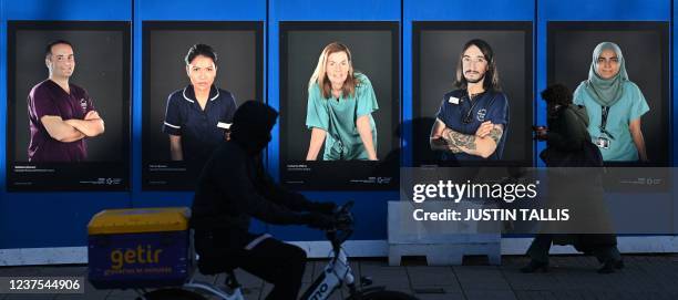 Pedestrians walk past images of workers of Britain's National Health Service fixed to hoardings outside a temporary field hospital, set up in the...