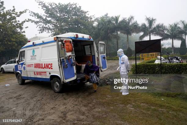 Healthcare worker wearing personal protective equipment stands next to a patient suffering from coronavirus , as she comes out of an ambulance at a...