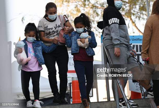 Two girls carry stuffed animal toys wearing face masks as they leave a Covid-19 screening at a testing and vaccination site at public school in Los...