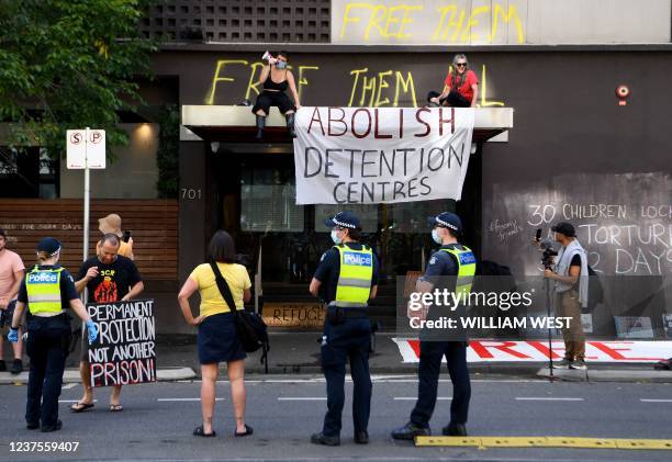 Pro-refugee activists sit on an awning over the hotel entrance where Serbia's tennis player Novak Djokovic is reported to be staying along with...