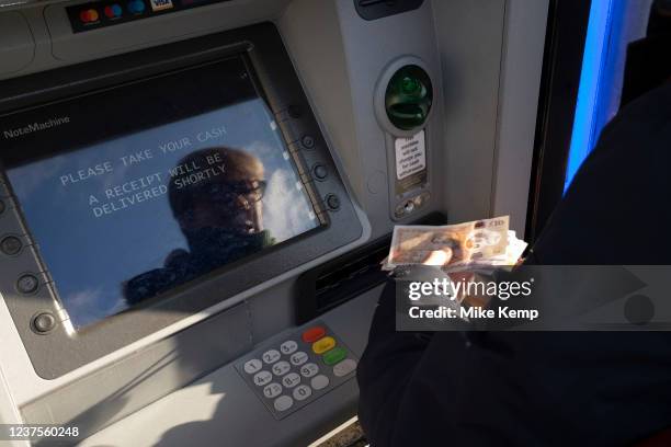 Woman withdraws cash from her bank by using a cashpoint machine on 10th December 2021 in Birmingham, United Kingdom. ATM machines aka automated...