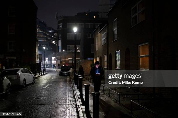 Man's face is lit up by the light from his smartphone at night as he is walking along Roupell Street on 7th December 2021 in London, United Kingdom.