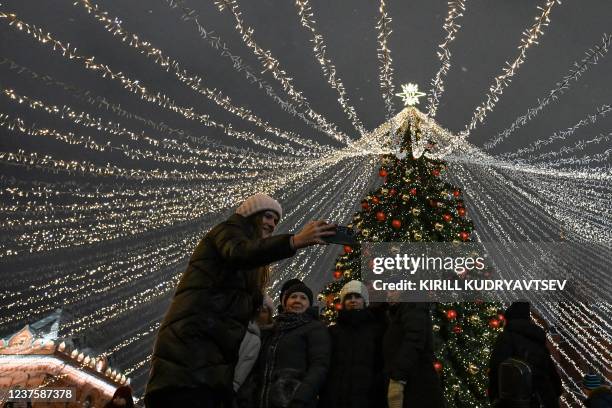 Woman makes a selfie with children by a Christmas tree under light snowfall during the Christmas holidays in Moscow on January 7, 2022. - Orthodox...