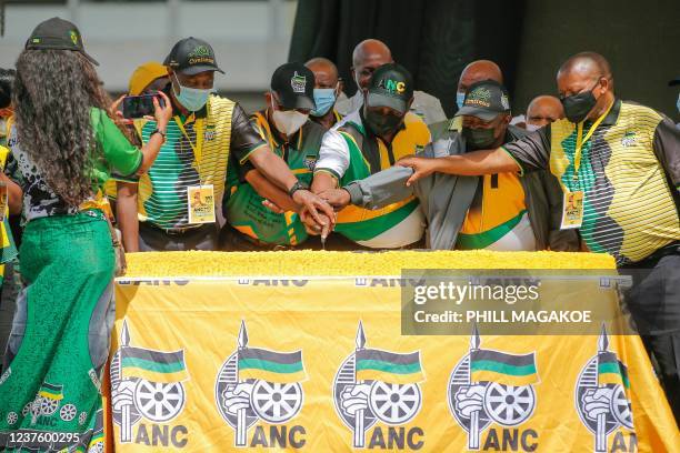 South Africa's President and African National Congress party's President Cyril Ramaphosa is assisted by other members to cut the birthday cake during...