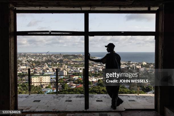 Man looks out over the city from an old bedroom window in the dilapidated Ducor hotel in Monrovia on November 18, 2021. - The Ducor Hotel, when it...