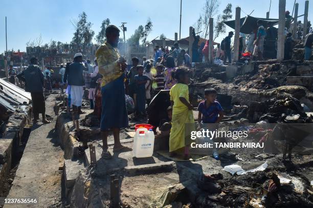 People gather on the ground of brunt-out houses a day after a fire gutted parts of a Rohingya refugee camp in Ukhia on January 10, 2022.