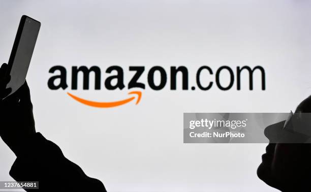 An image of a woman holding a cell phone in front of an Amazon.com logo displayed on a computer screen. On Tuesday, January 12 in Edmonton, Alberta,...