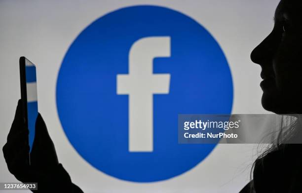 An image of a woman holding a cell phone in front of a Facebook logo displayed on a computer screen. On Tuesday, January 12 in Edmonton, Alberta,...