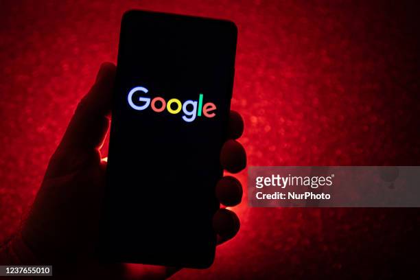 Google logotype on a smartphone held by a hand with a dark red background. Google closeup logo displayed on a phone screen, smartphone the logo or...