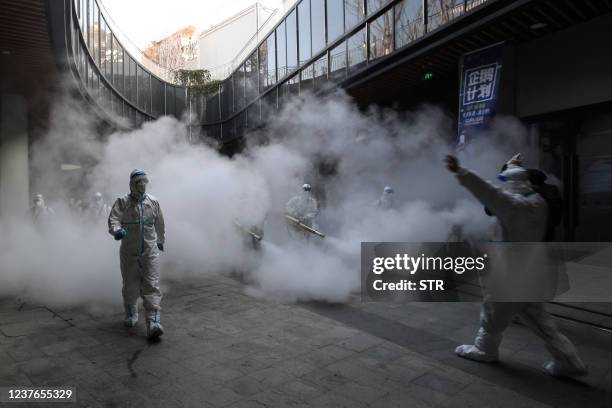 Staff members wearing personal protective equipment spray disinfectant outside a shopping mall in Xi'an in north China's Shaanxi province on January...