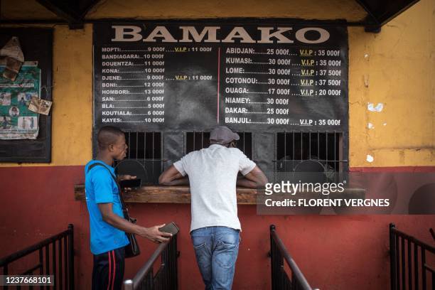 Men talk with a ticket seller at a bus station whilst waiting for cross boarder transport to resume in Bamako on January 11, 2022. - Since the...