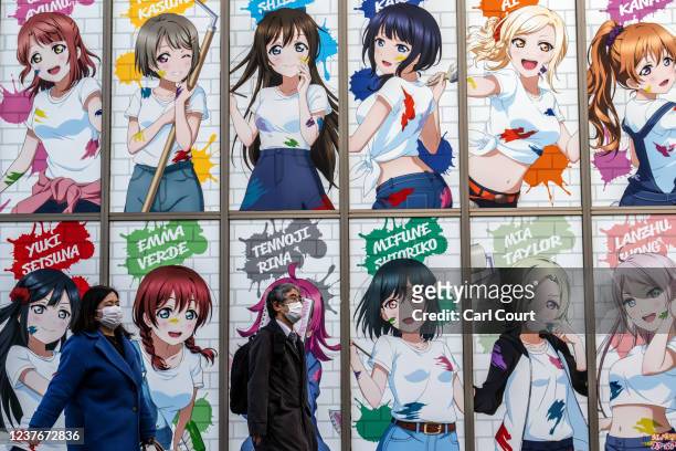 January 12: People wearing face masks walk past an advertising poster featuring manga characters on January 12, 2022 in Tokyo, Japan. Tokyo...