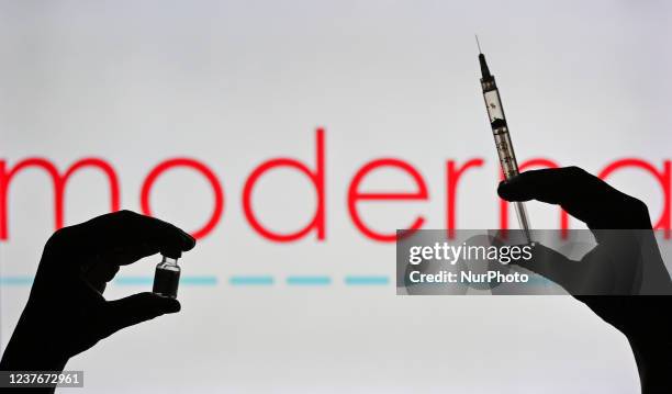 An illustrative image of a person holding a medical syringe and a Covid-19 vaccine vial in front of the Moderna logo displayed on a screen. On...